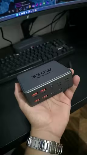 PowerNorth 330W charging station held in hand in front of a desk setup with monitor and keyboard